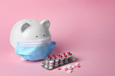 Photo of Piggy bank in face mask and pills on pink background, space for text. Medical insurance
