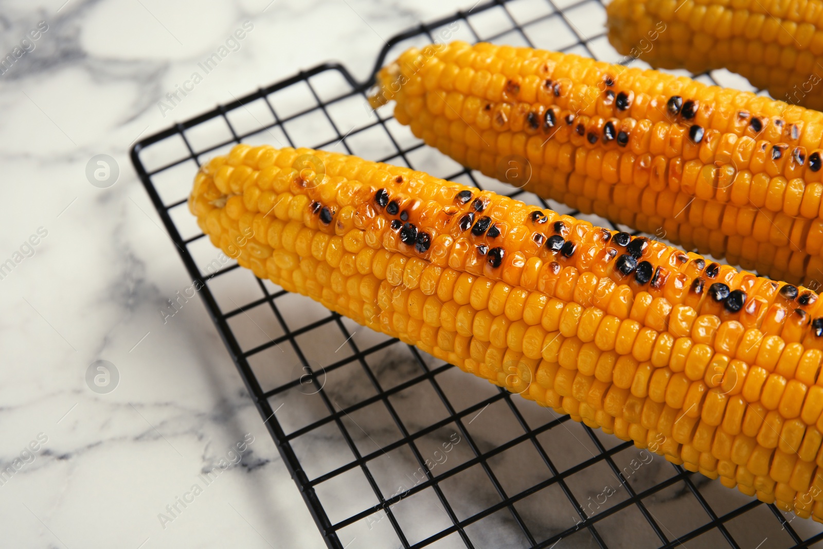 Photo of Cooling rack with grilled corn cobs on marble background, closeup