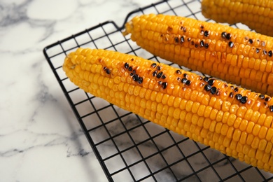 Photo of Cooling rack with grilled corn cobs on marble background, closeup