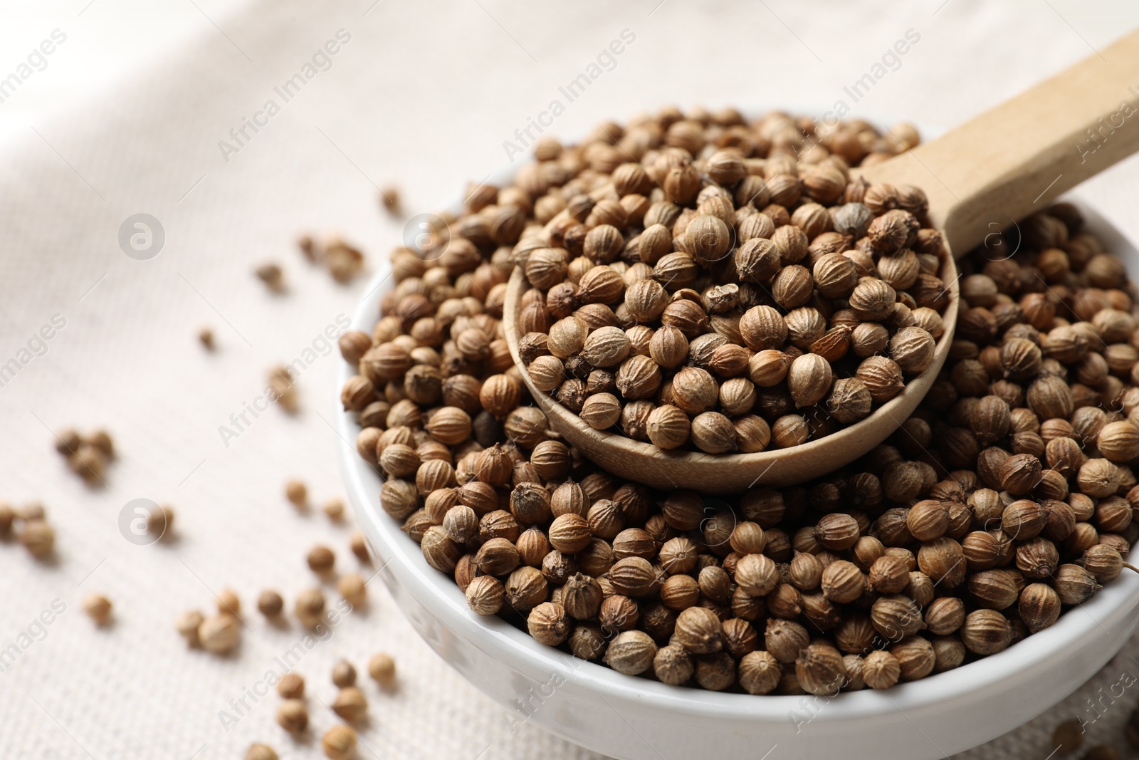 Photo of Dried coriander seeds in bowl and spoon on light table, closeup