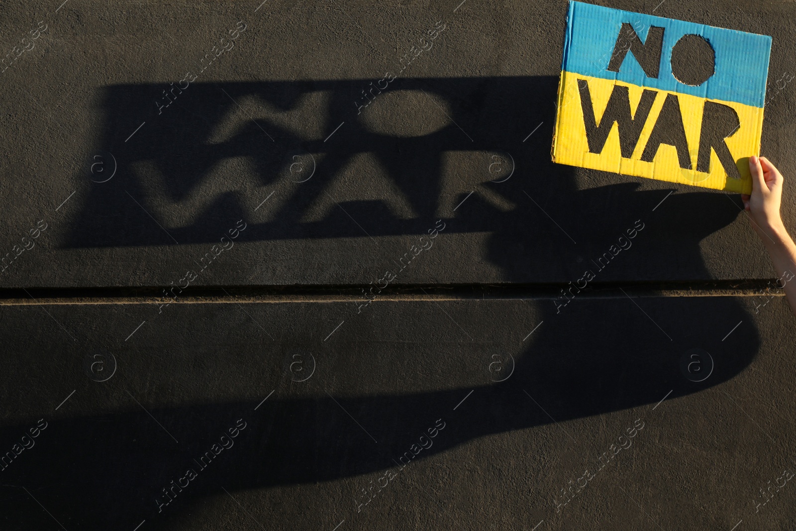 Photo of Woman holding poster with words No War near grey stone wall, closeup