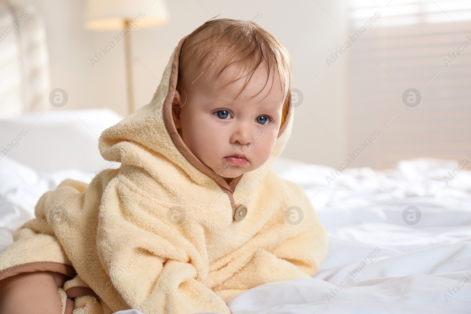 Photo of Cute little baby in yellow hooded towel on bed after bath