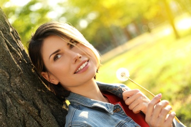 Young woman with dandelion in park on sunny day. Allergy free concept