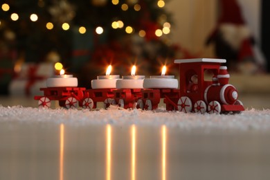 Toy train with burning candles near Christmas tree in room, closeup