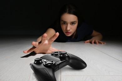 Image of Gaming disorder. Woman reaching out for gamepad on floor from darkness