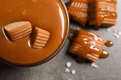 Photo of Tasty salted caramel with candies in glass bowl on grey table, top view