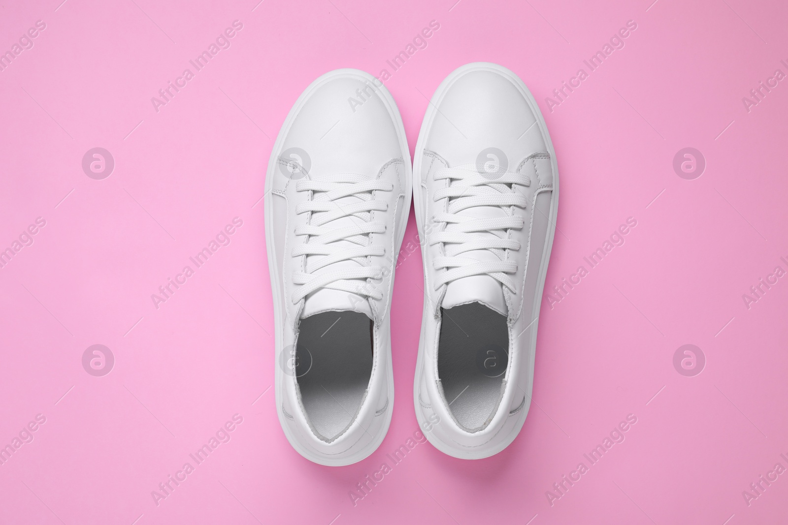 Photo of Pair of stylish white sneakers on pink background, top view