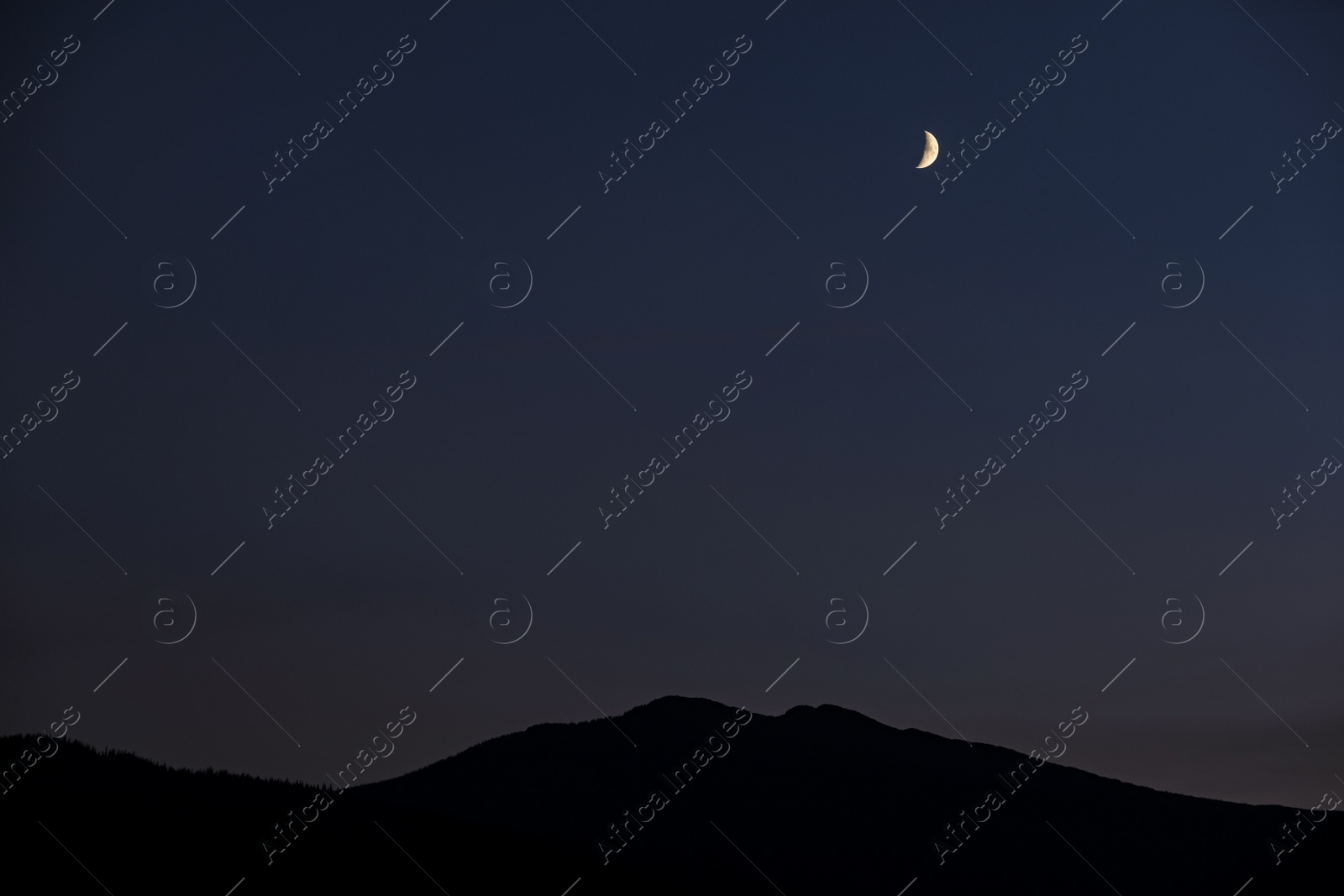 Photo of Bright crescent in dark sky over mountains