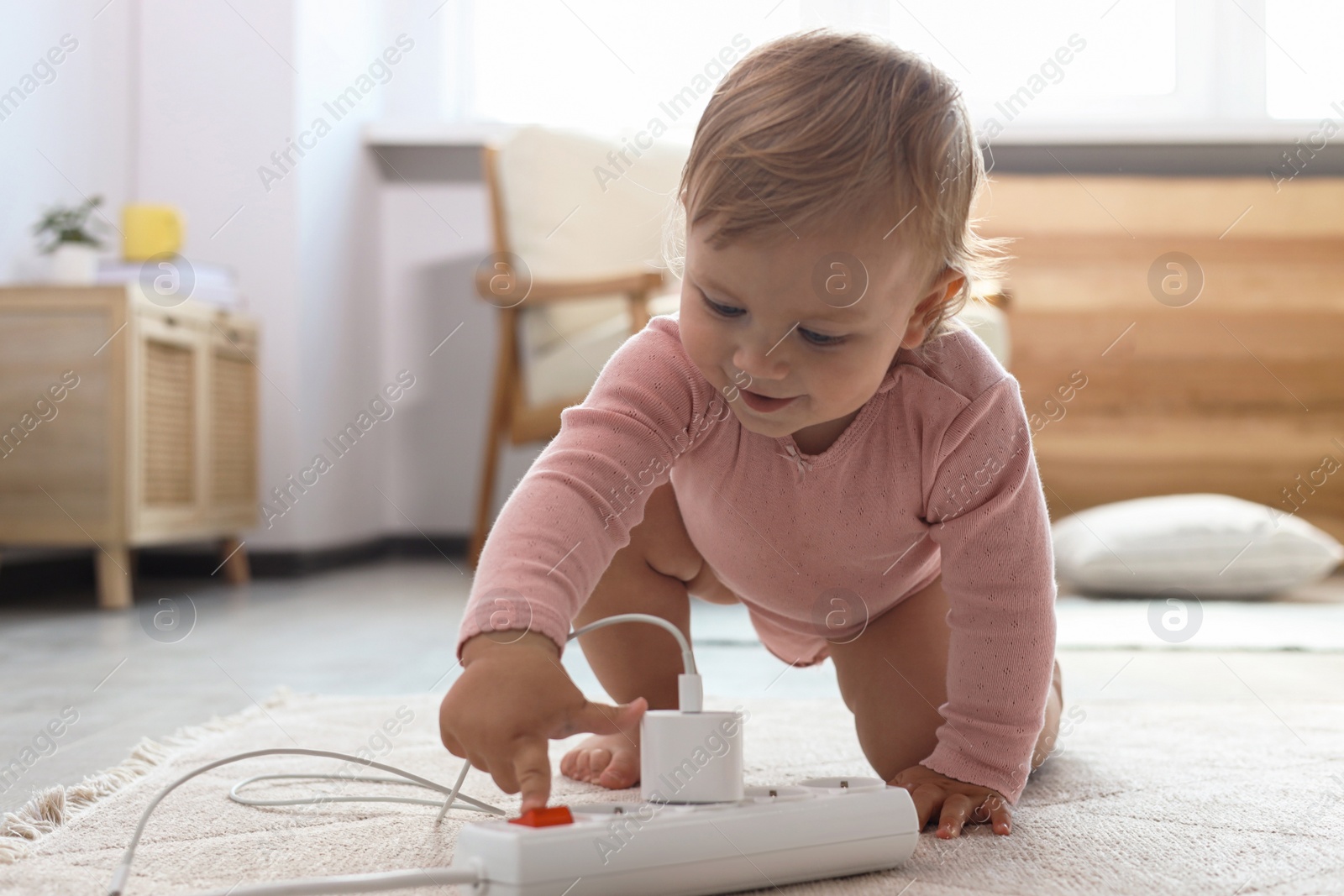 Photo of Cute baby playing with power strip on floor at home. Dangerous situation