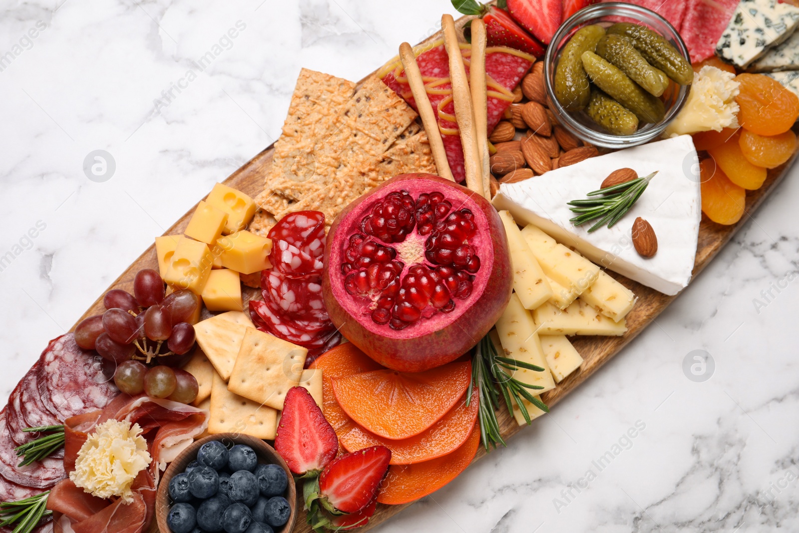 Photo of Wooden plate with different delicious snacks on white marble table, top view