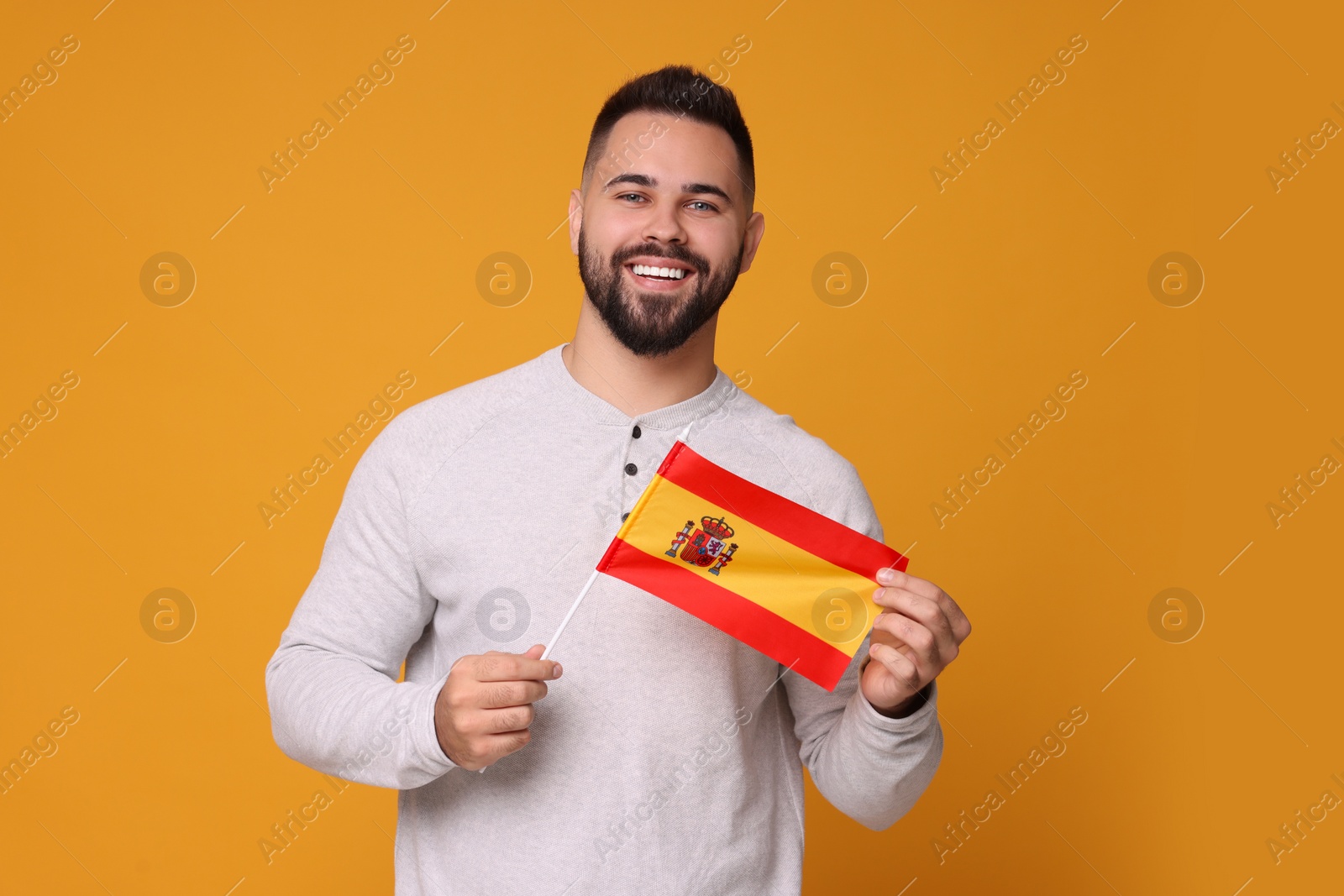 Photo of Young man holding flag of Spain on orange background