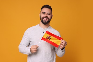 Photo of Young man holding flag of Spain on orange background
