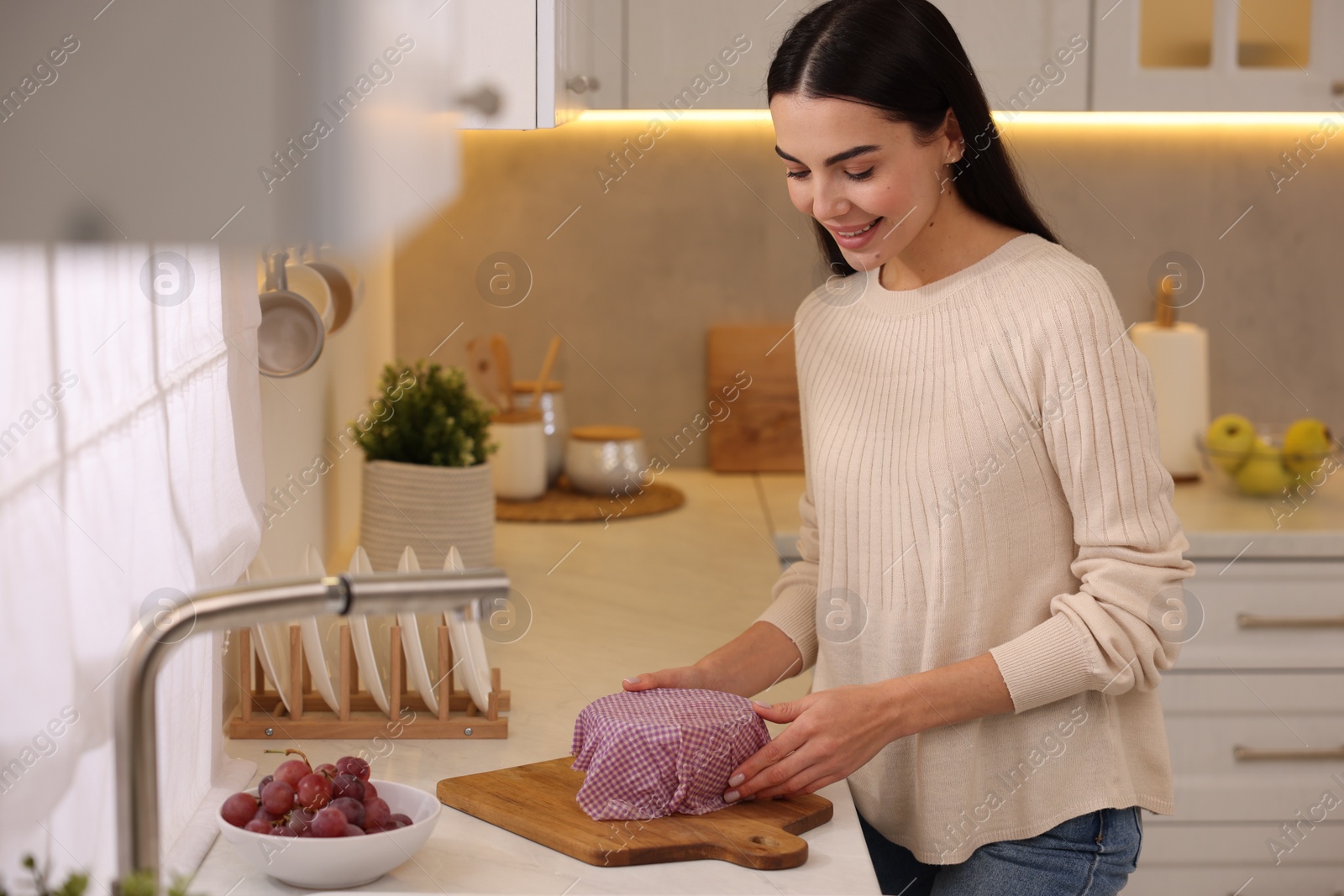 Photo of Happy woman packing bowl into beeswax food wrap at countertop in kitchen