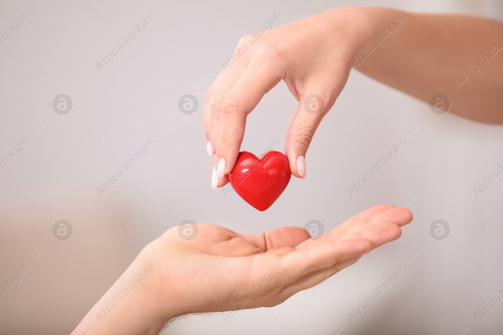 Photo of Woman giving red heart to man on blurred background, closeup. Donation concept