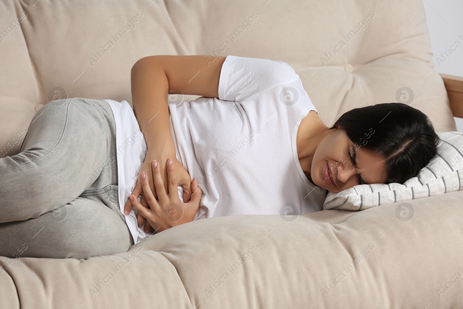 Photo of Young woman suffering from menstrual pain on sofa indoors