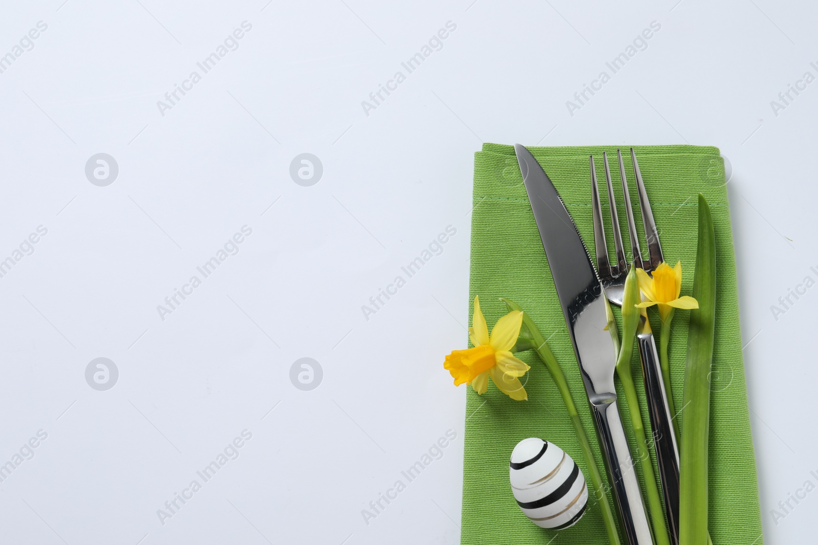 Photo of Cutlery set, Easter egg and narcissuses on white background, top view with space for text. Festive table setting