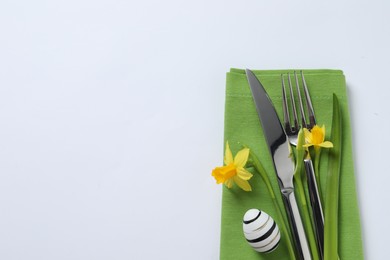 Photo of Cutlery set, Easter egg and narcissuses on white background, top view with space for text. Festive table setting