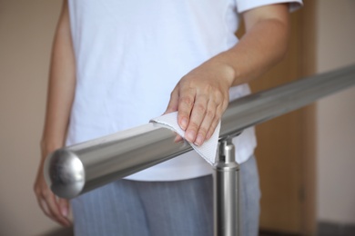 Photo of Woman cleaning metal railing with tissue paper, closeup