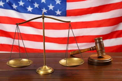 Photo of Scales of justice and gavel on wooden table against American flag