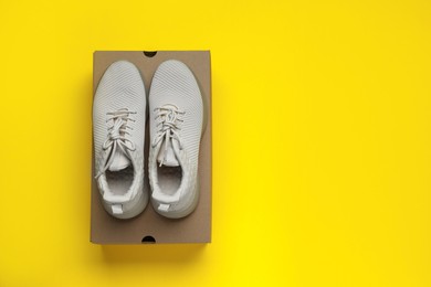 Photo of Comfortable sports shoes with cardboard box on yellow background, top view. Space for text