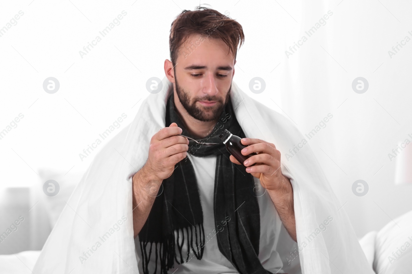 Photo of Ill young man taking cough syrup indoors