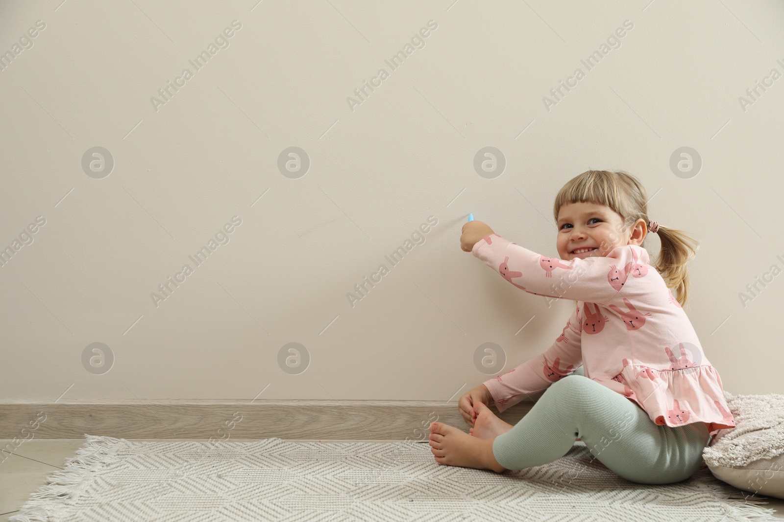 Photo of Little girl drawing on beige wall indoors, space for text. Child`s art