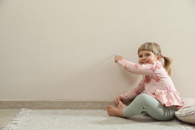 Little girl drawing on beige wall indoors, space for text. Child`s art