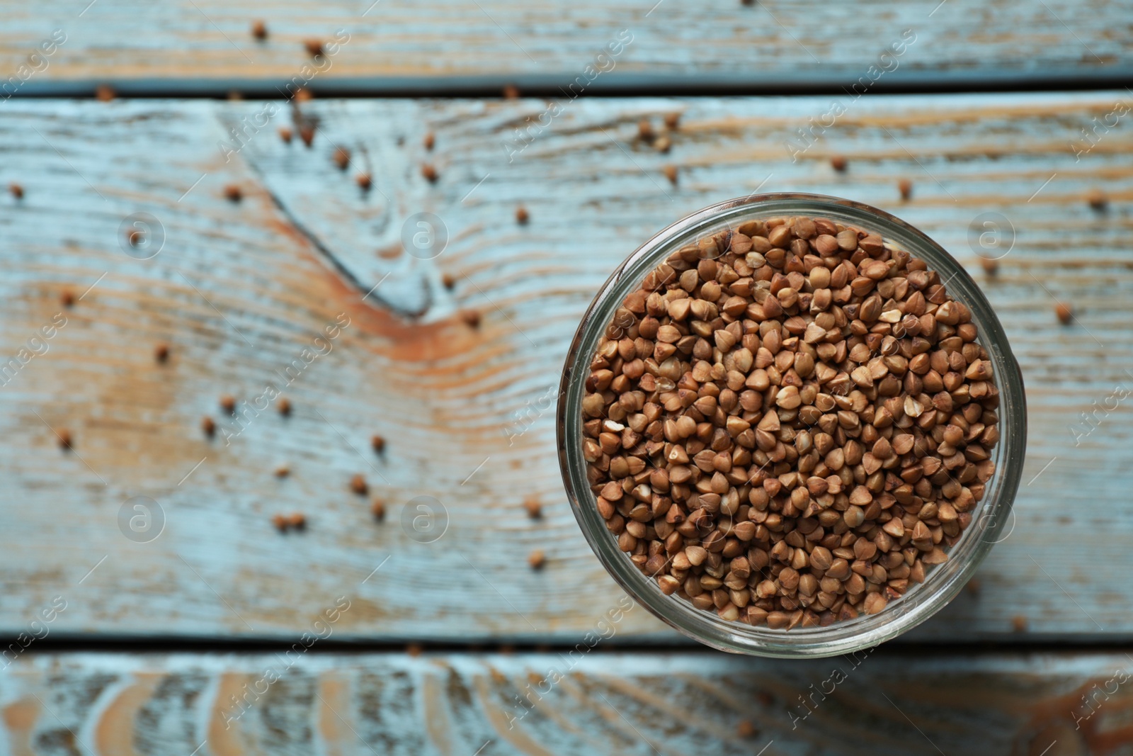 Photo of Uncooked buckwheat in glass on table, top view. Space for text