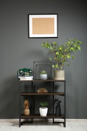 Vintage green telephone, books and houseplants on console table near grey wall indoors