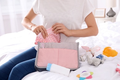 Woman packing baby accessories into maternity bag on bed, closeup