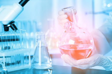 Scientist holding Florence flask with liquid at table, closeup. Laboratory analysis