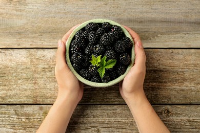 Photo of Woman putting bowl of fresh ripe black blackberries on wooden table, top view