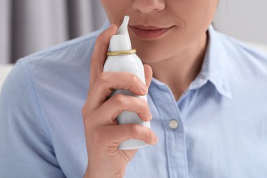 Photo of Woman using nasal spray on blurred background, closeup
