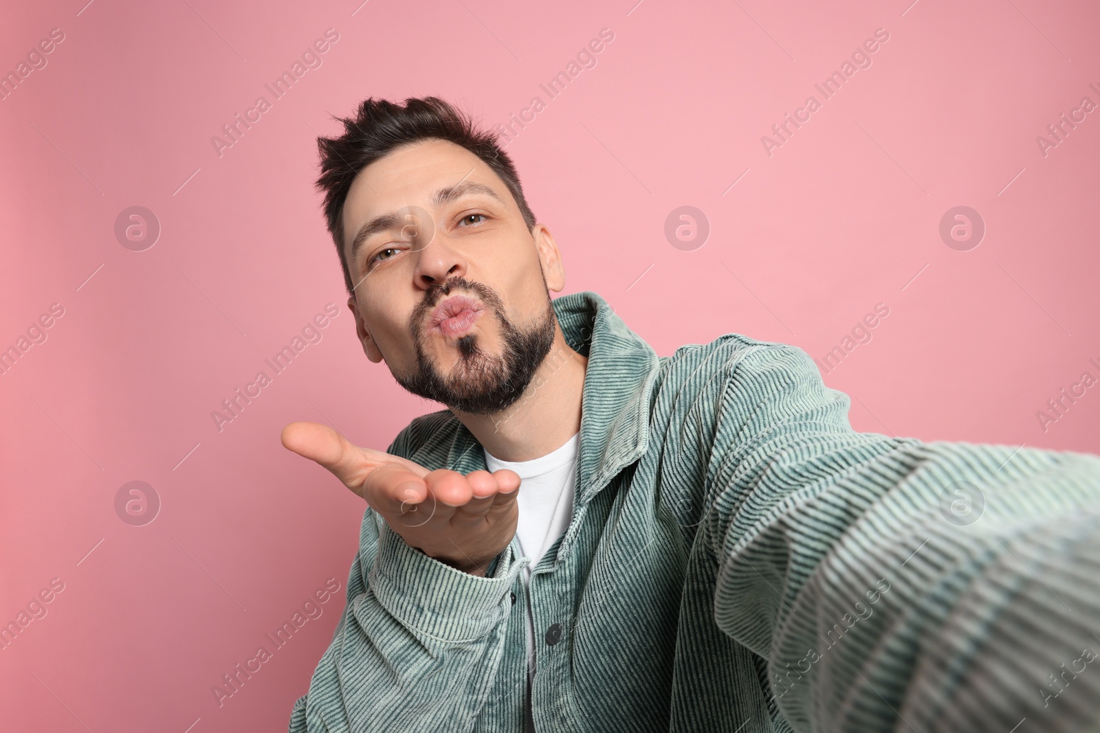 Photo of Handsome man blowing kiss while taking selfie on pink background