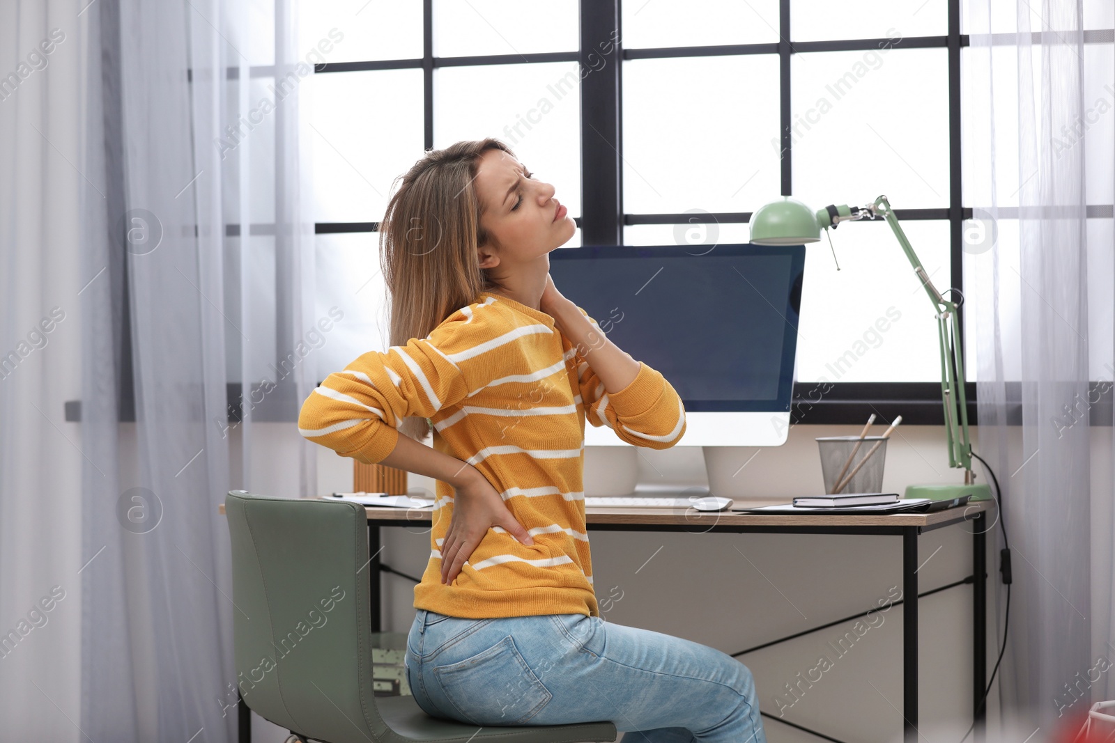 Photo of Young woman suffering from back pain in office