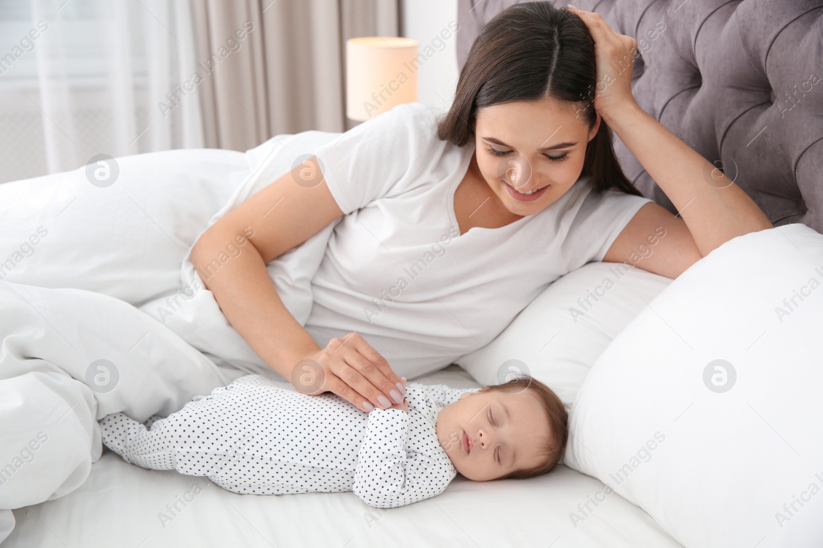 Photo of Happy woman with her sleeping baby on bed