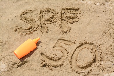 Photo of Abbreviation SPF 50 written on sand and blank bottle of sunscreen at beach, above view
