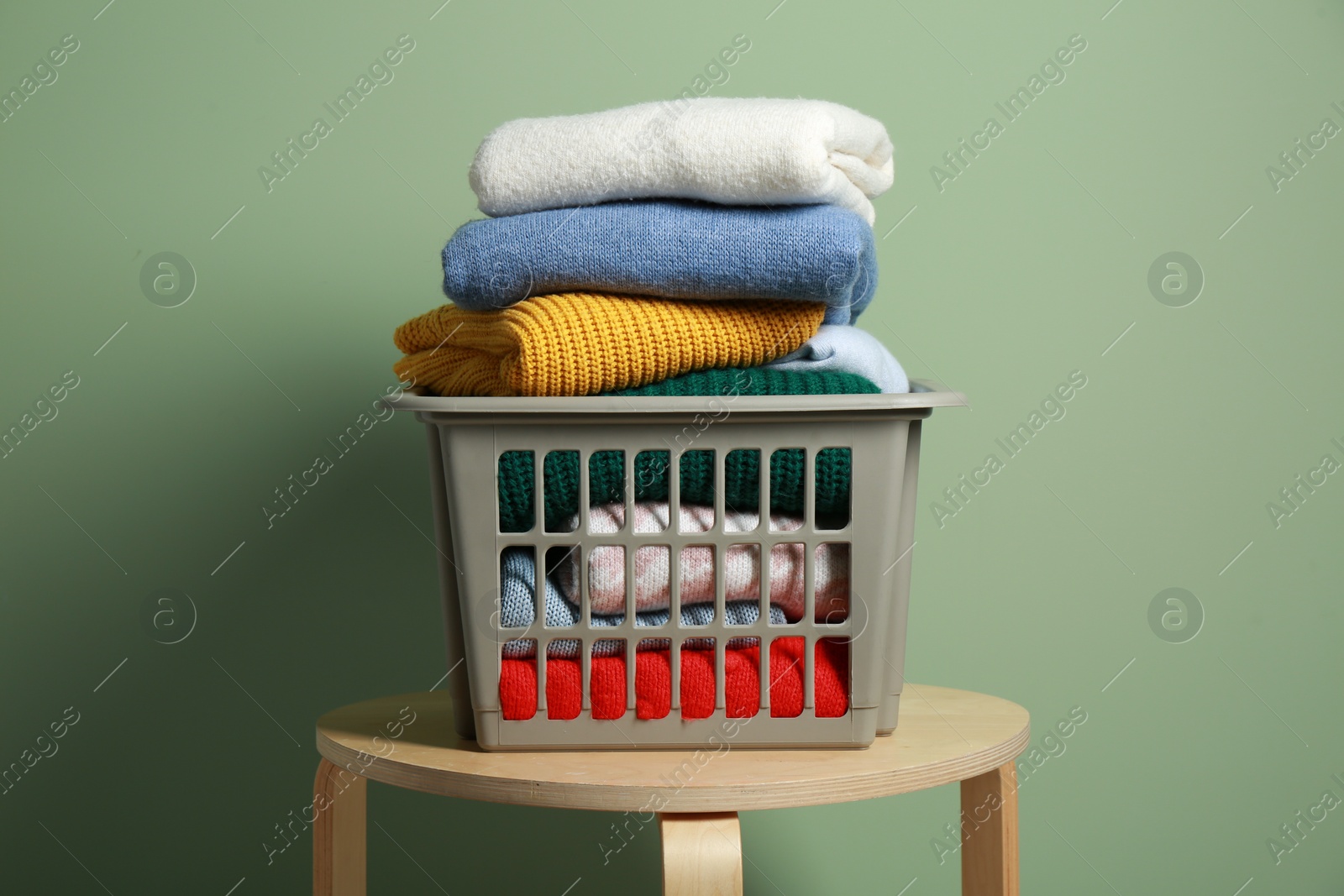 Photo of Plastic laundry basket with clean clothes on wooden table near light green wall