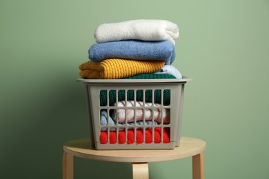 Photo of Plastic laundry basket with clean clothes on wooden table near light green wall