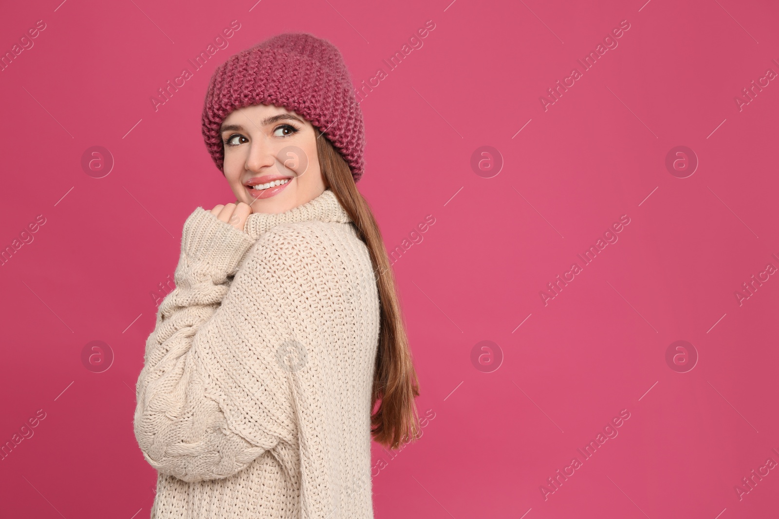 Photo of Young woman wearing warm sweater and hat on crimson background. Winter season