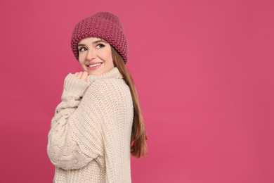 Young woman wearing warm sweater and hat on crimson background. Winter season