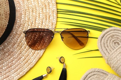 Photo of New stylish sunglasses, straw hat, earrings and wicker slippers on yellow background, flat lay