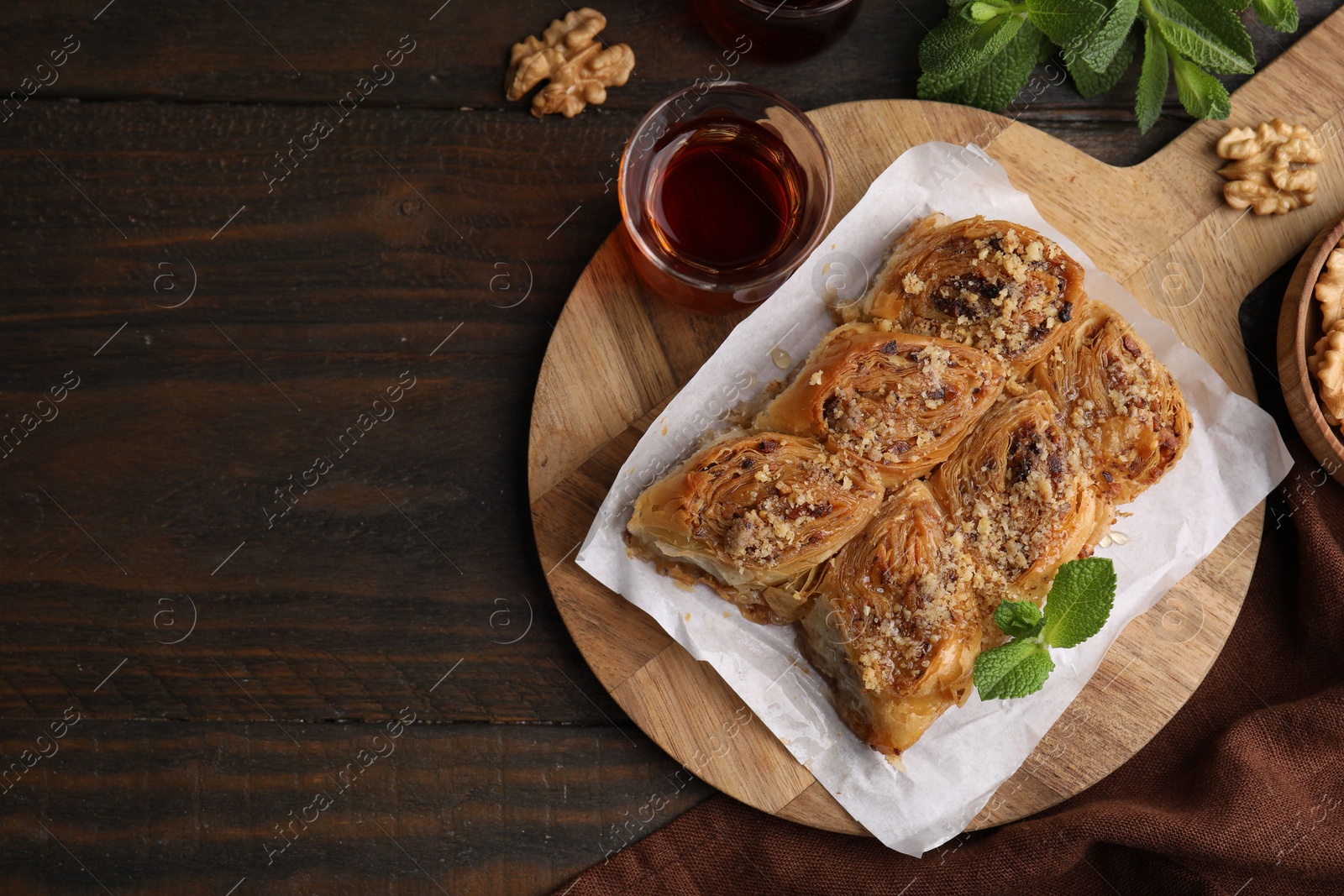 Photo of Eastern sweets. Pieces of tasty baklava, walnuts and tea on wooden table, flat lay. Space for text