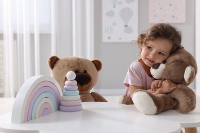 Cute little girl with teddy bears and toys at white table in room
