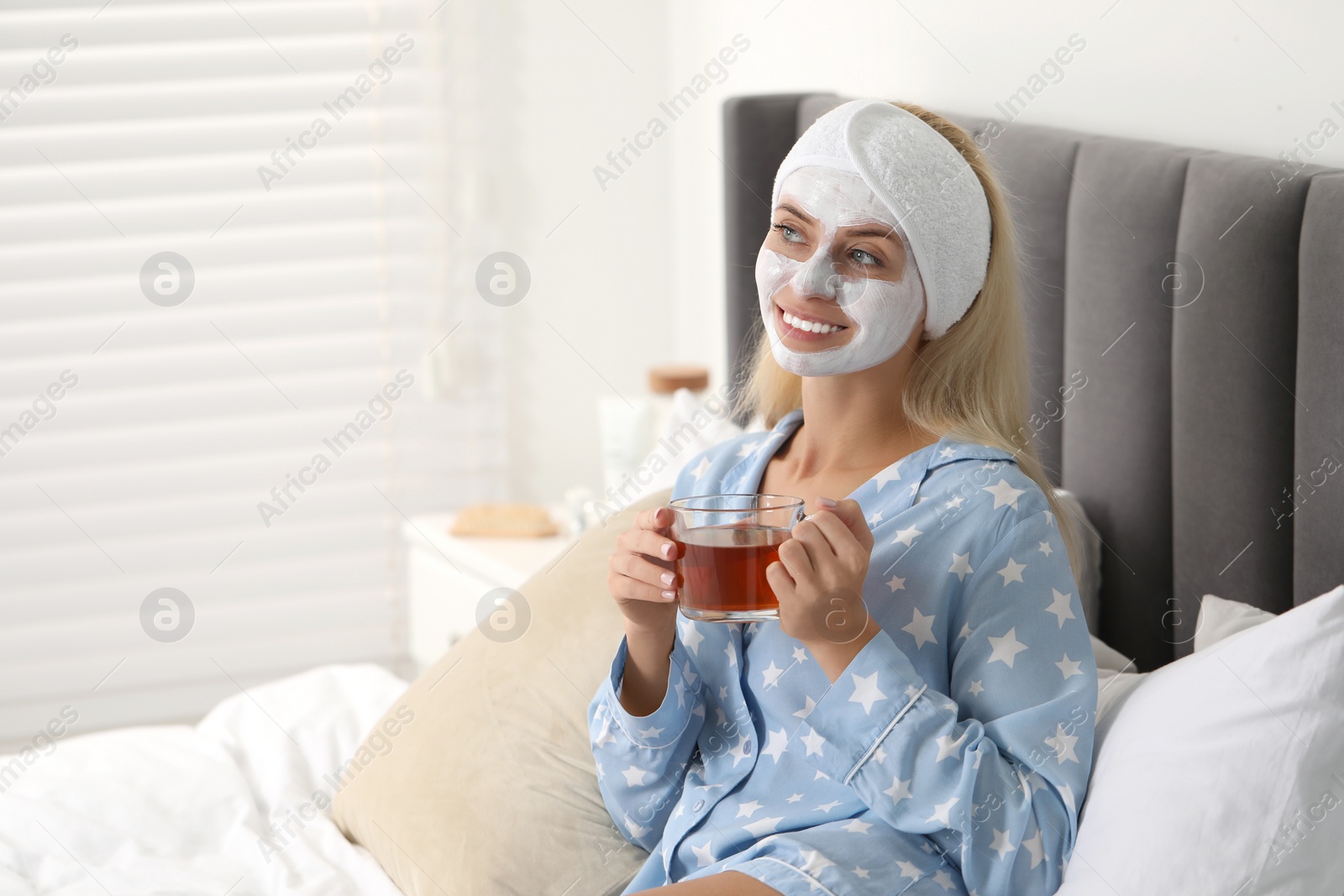 Photo of Young woman with face mask drinking tea on bed at home, space for text. Spa treatments