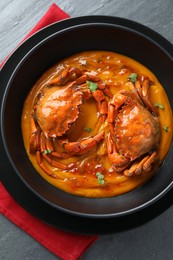 Photo of Delicious boiled crabs with sauce in bowl on grey textured table, top view