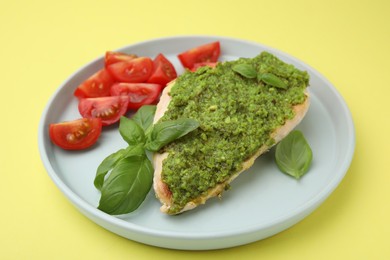 Delicious chicken breast with pesto sauce, tomatoes and basil on yellow table, closeup