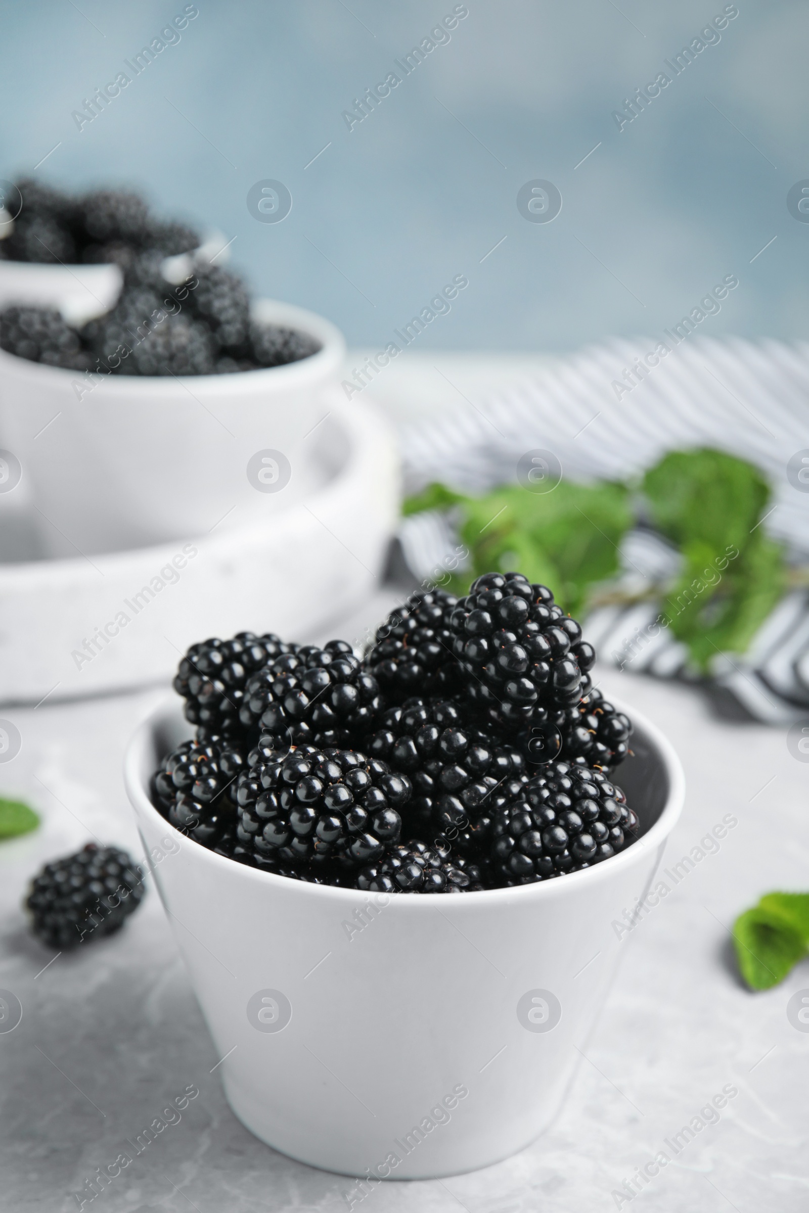 Photo of Bowl of tasty blackberries on grey marble table, space for text
