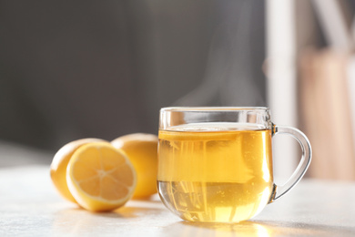 Photo of Glass cup of tea with lemon on white table against blurred background, space for text. Winter drink