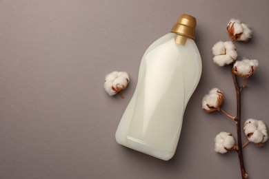 Photo of Bottle of fabric softener and beautiful cotton flowers on gray background, flat lay. Space for text